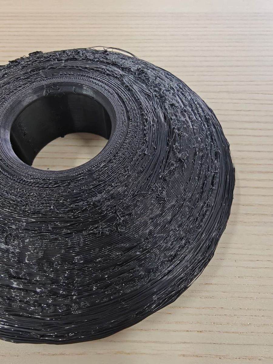 Close-up of a black 3D printed part with stringy, rough overhang surfaces and loose filament strands